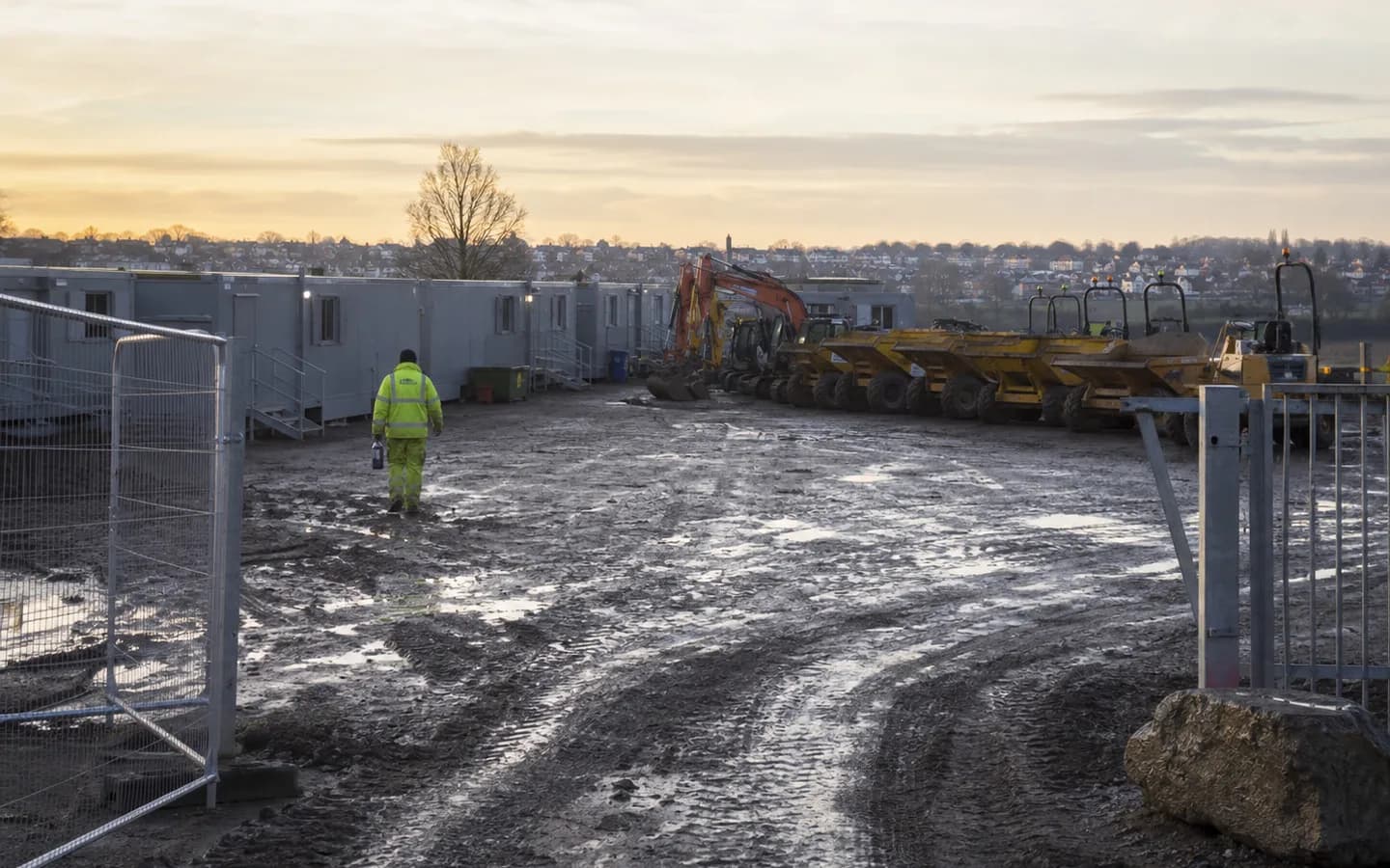 A UK groundworks compound at first light — welfare cabins, parked plant and a muddy haul road